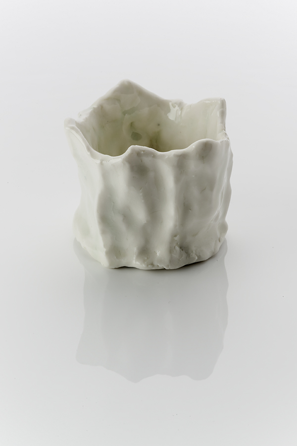 A cylindrical ceramic vessel made from a white clay body, washed over with a shiny glaze. The form is dimpled, roughly-made and unsteady with finger markings . The rim of the vessel is undulated and uneven