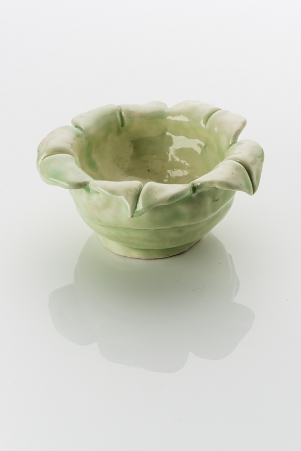 Hand made ceramic bowl made from a white clay body, washed over with a pale green shiny glaze. The rim of the bowl opens up with leaf like petals