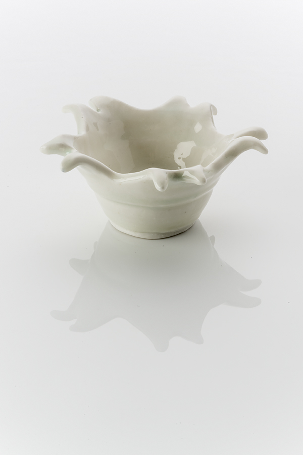 Hand made ceramic bowl made from a white clay body, washed over with a pale shiny glaze. The rim of the bowl erupts like a splashed puddle of water in freeze frame.
