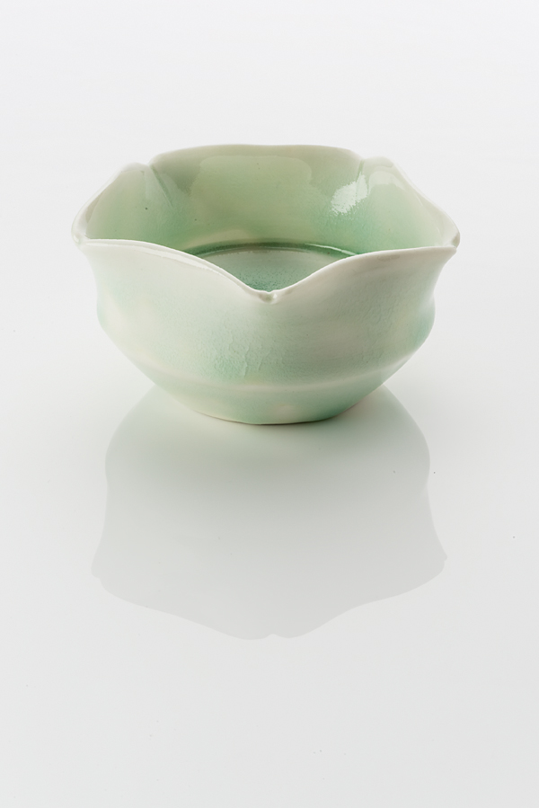Hand made ceramic bowl made from a white clay body, washed over with pale green shiny glaze. The rim curves opens slightly at five equal points, rendering the gesture of a flowering bloom.