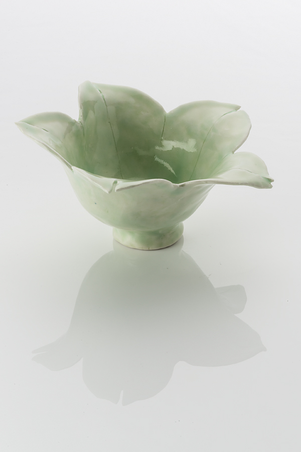 Hand made ceramic bowl made from a white clay body, washed over with a pale green shiny glaze. The base of the form has a narrow foot ring, while the rim flowers open with leaf-like petals.