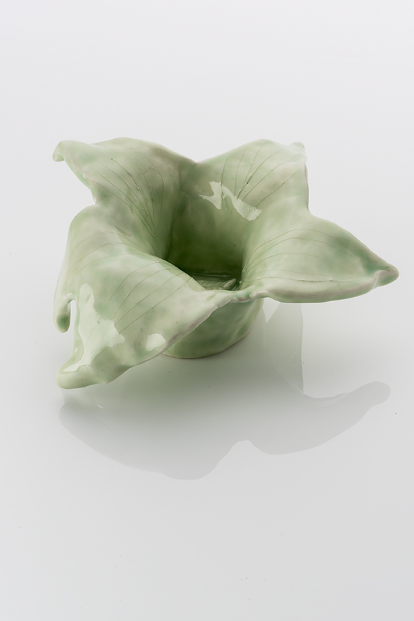 Hand made ceramic form in the shape of a flowering bloom comprising of five broad leaf-like petals. The object is made from a white clay body, washed over with a pale green shiny glaze. The rim of the bowl opens up with leave like petals.