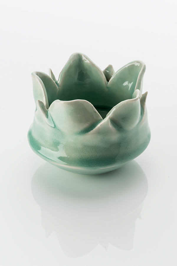 Hand made ceramic bowl in the shape of an opened lotus bloom. The object is made from a white clay body, washed over with what looks like a green celdon glaze.