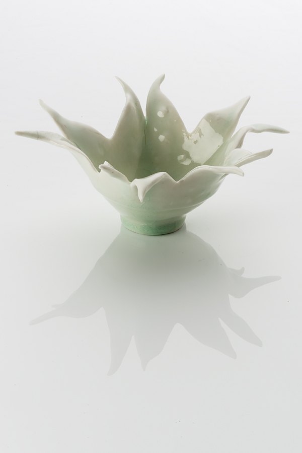 Hand made ceramic flowering form made from a white clay body, washed over with a pale green shiny glaze. The base of the form has a foot ring which slightly flairs into a bowl, before opening up wildly with 10 pointed petals.